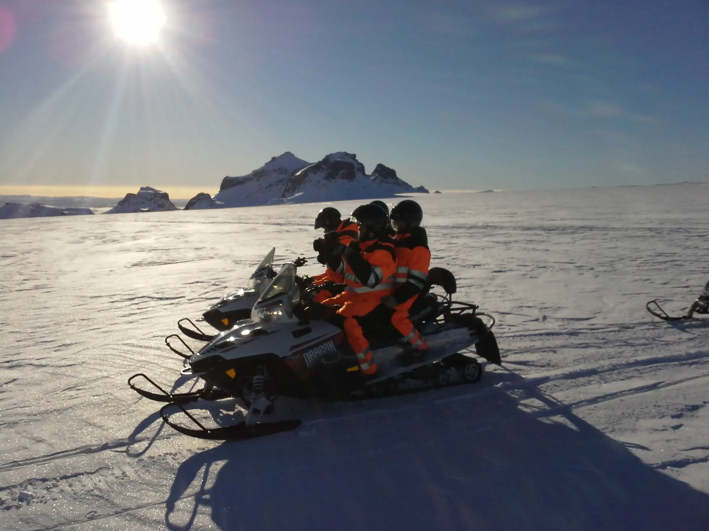 Snowmobiles on the glacier with the sun low in the sky
