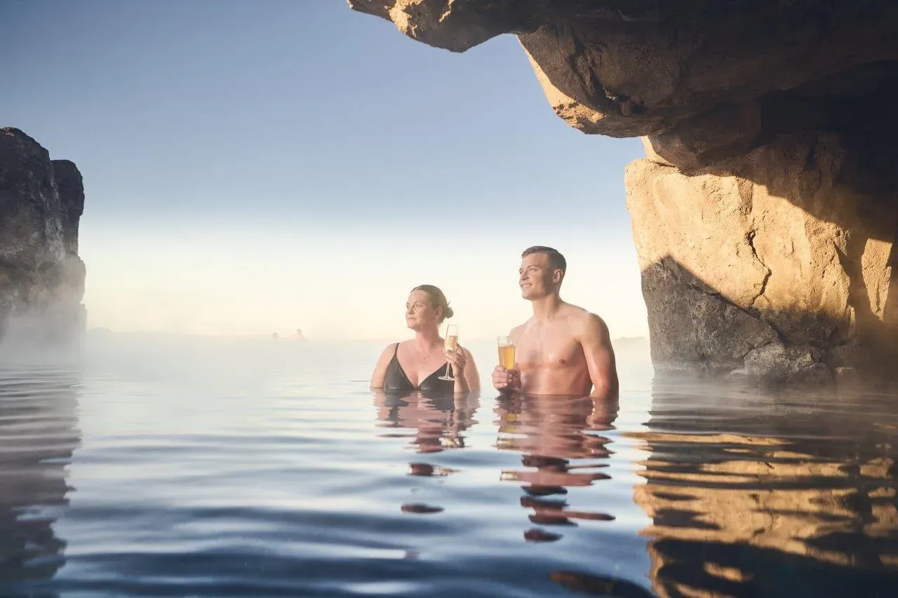 Couple with drinks in the Sky Lagoon pool beside a rock wall