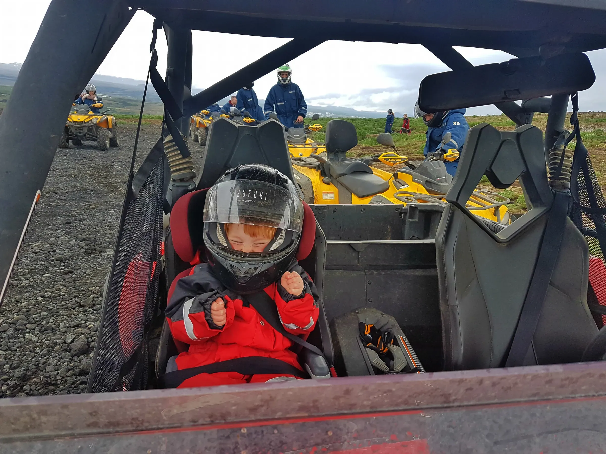 Child in a helmet and red overalls sitting in a buggy
