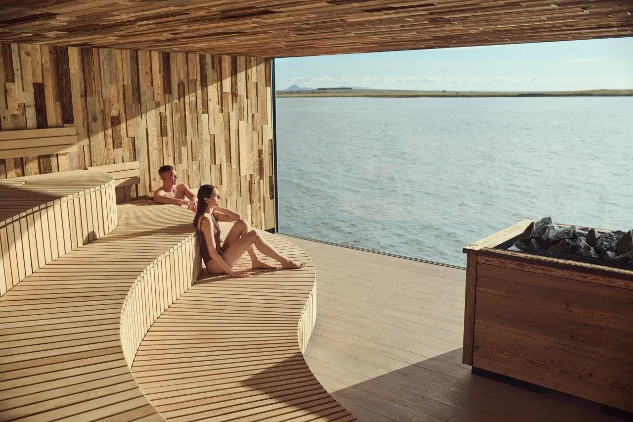 Guests relaxing on wooden benches by the sea-view window at Sky Lagoon