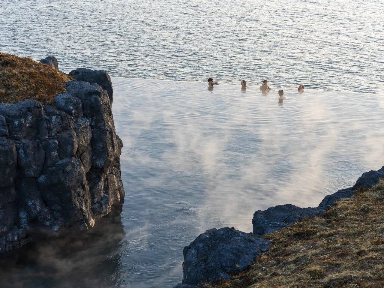 Bathers at the infinity edge of Sky Lagoon above the ocean