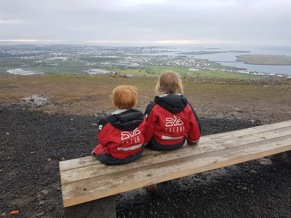 Two children in red overalls on a bench overlooking Reykjavík