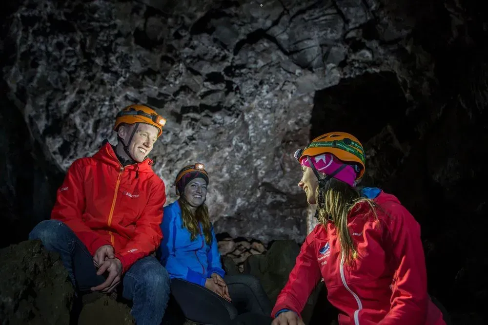 Three cavers with helmets and headlamps sitting inside a lava cave
