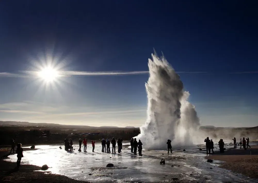 Strokkur geyser erupting with visitors watching against the sun