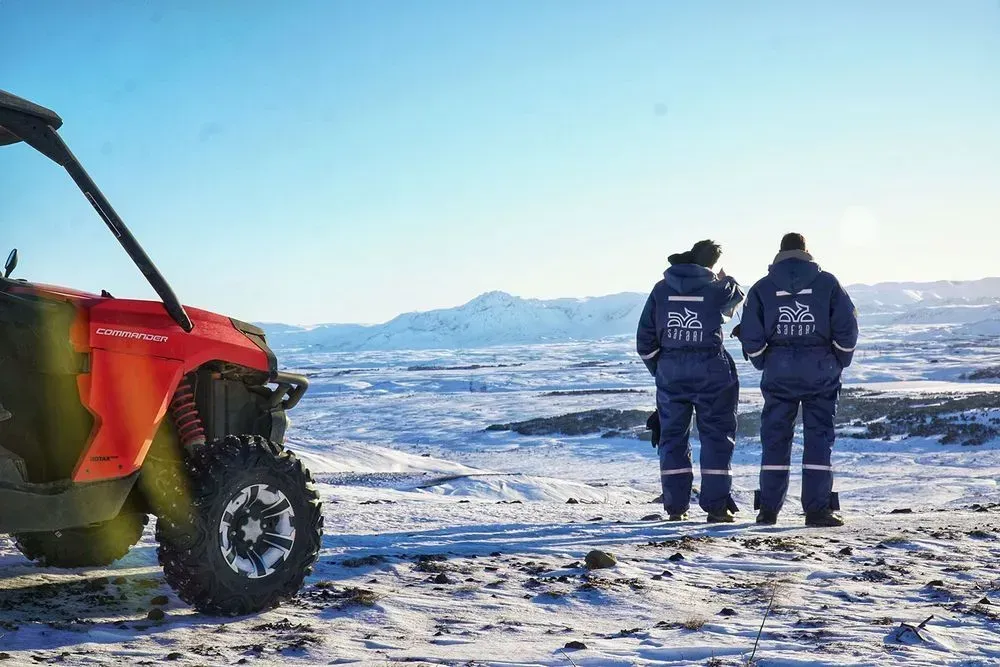 Two riders in blue overalls looking over a snowy landscape beside a red buggy