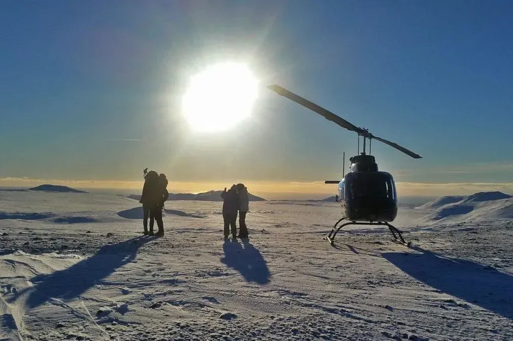 Passengers in the snow beside a helicopter on a mountain landing