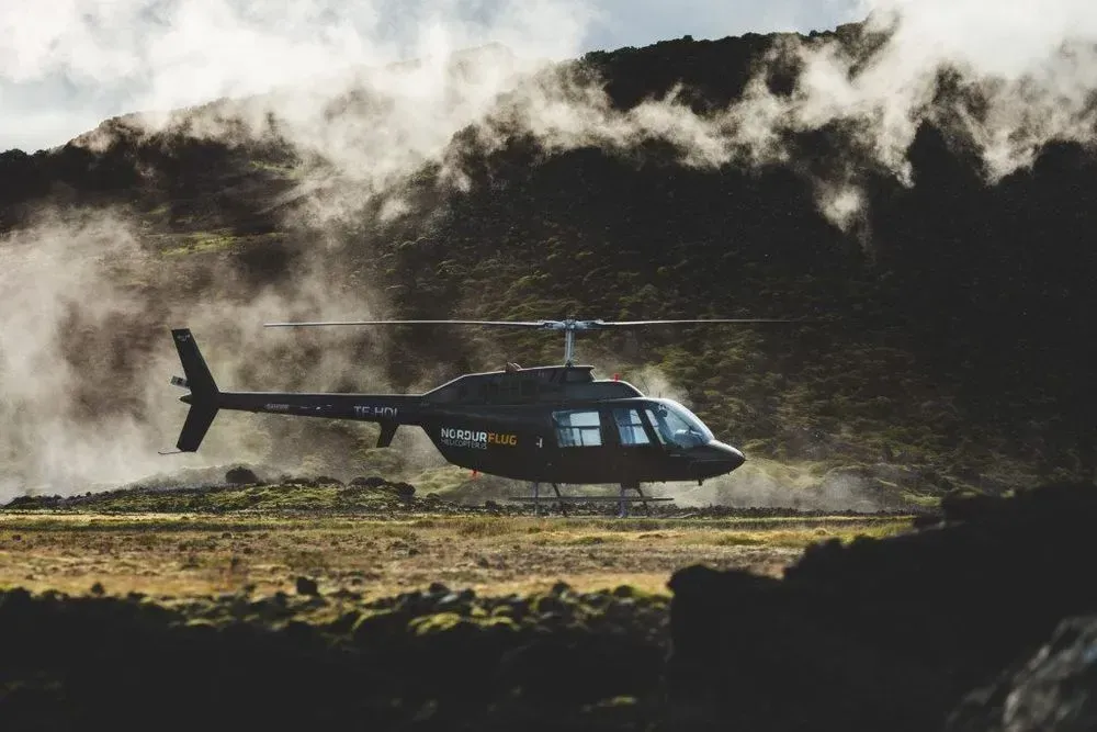 Helicopter flying low past steaming geothermal hills