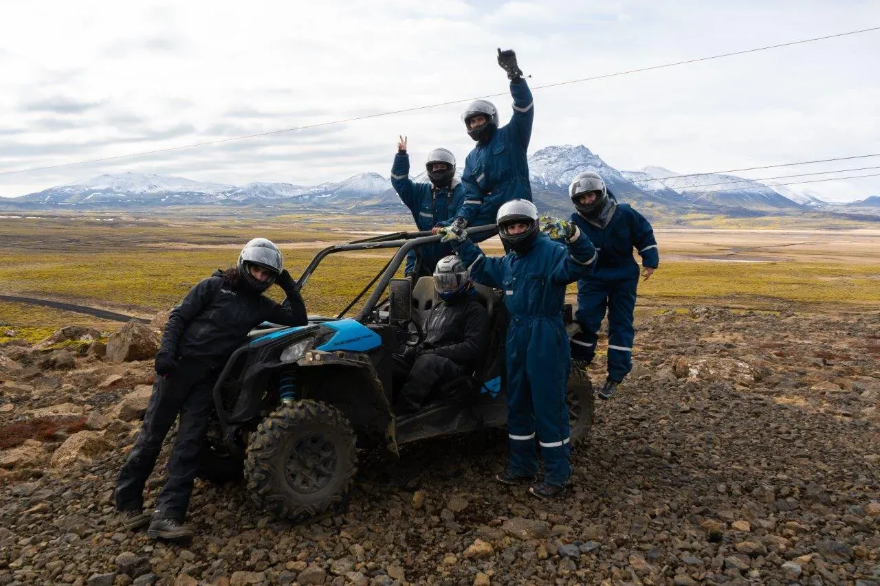 Group in helmets and overalls cheering around a blue buggy with snowy mountains behind