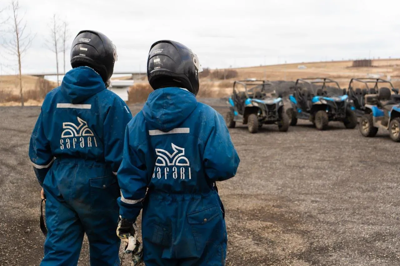 Two riders in blue overalls and helmets walking towards a row of buggies