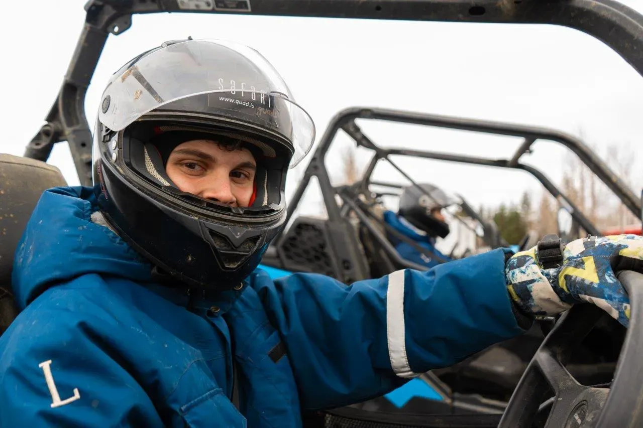 Smiling driver in a helmet and blue overalls at the wheel of a buggy