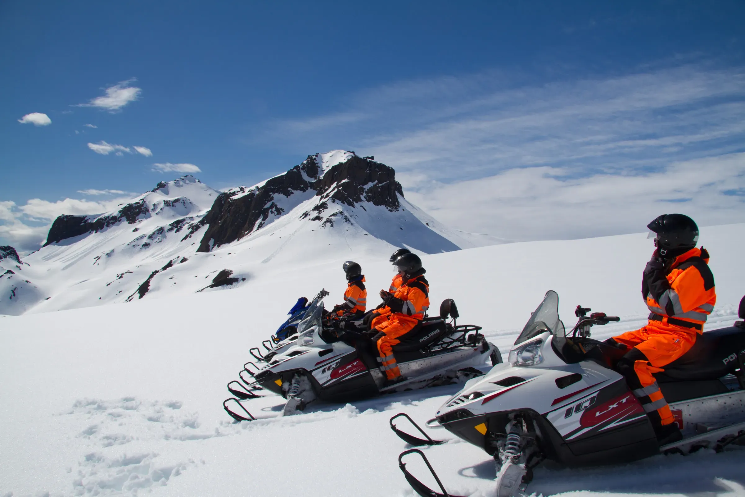 Snowmobiles on Langjökull glacier below a rocky peak