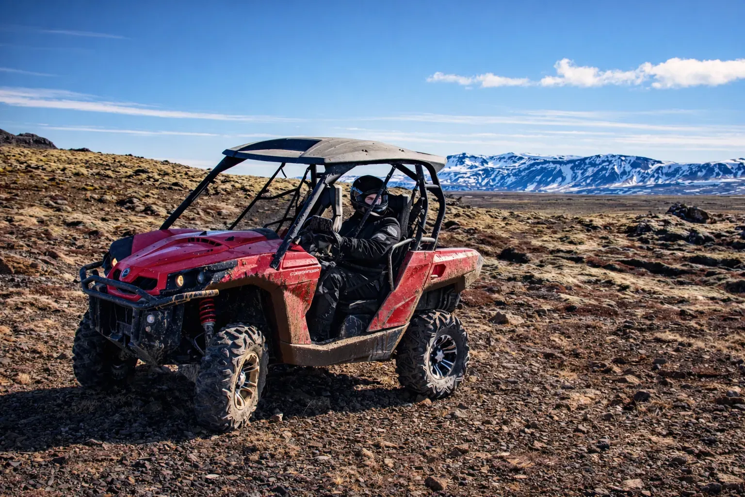 Red buggy parked on a lava plain with snowy mountains behind