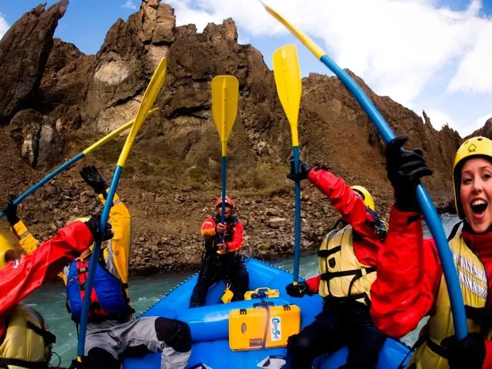 Rafters cheering with paddles raised below canyon cliffs