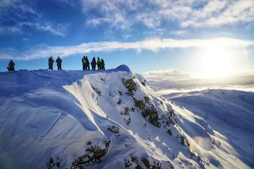 Group standing on a snowy mountain ridge in bright sunshine